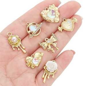 Golden alloy heart and rose charms with pearls and rhinestones held in hand for DIY jewelry