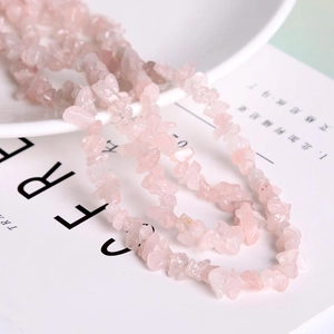 Natural rose quartz tumbled stone beads for DIY jewelry making on white ceramic plate