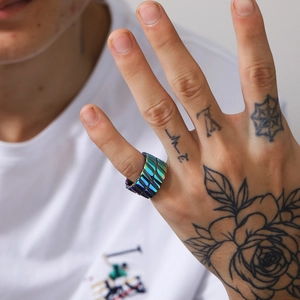 Nahaufnahme eines schillernden Titanstahlrings mit industriellem Schuppen-Design am Finger