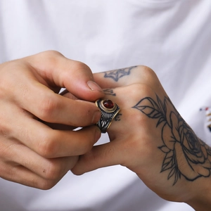 Detalle de anillo punk vintage con gema roja en mano de hombre con tatuajes