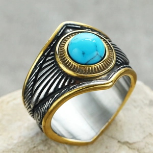 Detalle de piedra turquesa con bordes dorados y grabado de plumas en un anillo punk acero