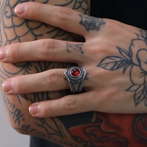 Primer plano de anillo punk vintage con gema roja y grabado de pluma en mano tatuada