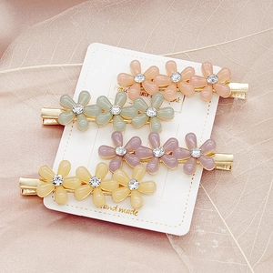 Détail macro de quatre barrettes à fleurs pastel avec centres en strass et métal doré