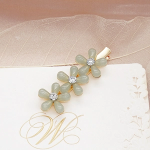 Détail de trois pinces à cheveux florales gris-vert avec cristaux sur base dorée