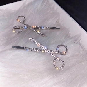 Set of two silver scissor-shaped hair clips with sparkling rhinestones on faux fur background