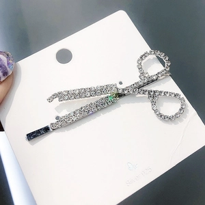Macro detail of scissor-shaped hair clip with shimmering rhinestones on silver card