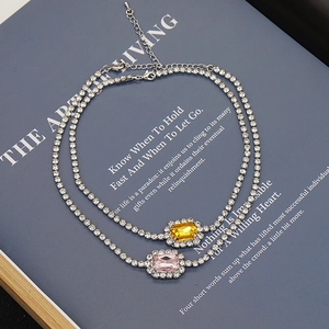 Collar de tenis plateado con colgantes de piedras rosas y amarillas sobre libro azul