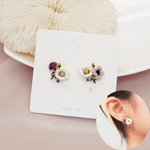 Detail of floral enamel earrings with white daisy and blue gemstone on S925 silver studs