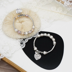 Detail eines Süßwasserperlenarmbands mit vintage Herzanhänger und Gravurdetails