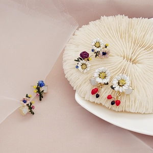 Close-up of artistic flower and berry enamel earrings on a coral display stand