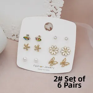 Detailed set of 6 pairs of earrings including swan, daisy, and pearl studs on a display card