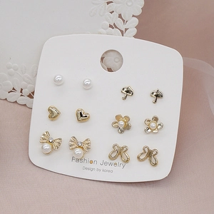 Close-up of 6 pairs golden stud earrings set with pearls and bows on display card
