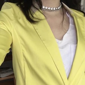 Detalle de una gargantilla de doble capa con diamantes de imitación sobre un blazer amarillo