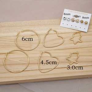 Detail view of gold hoop earring set with C-shape, heart and star designs on wood