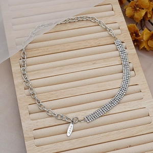 Detalle macro del collar plateado con filas de pedrería y etiqueta metálica con la marca MERX