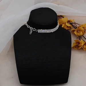 Detalle de collar de diamantes con eslabones plateados y placa MERK en soporte negro