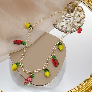 Détail d'un collier doré avec breloques fruits pastèque et cerise sur un miroir