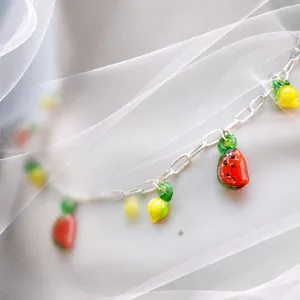 Collier de perles aux fruits colorés avec chaîne argentée sur fond de tulle blanc
