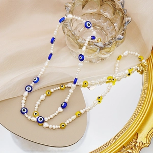 Detalle de collar de perlas barrocas con cuentas de ojo turco sobre superficie de espejo