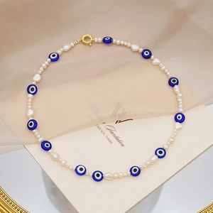 Detalle macro de collar de perlas barrocas con cuentas de ojo turco y cierre dorado
