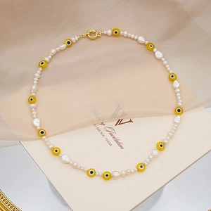 Detalle de collar de perlas barrocas con amuleto de ojo amarillo y cierre dorado