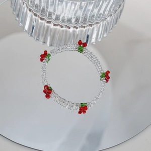 Détail d'un bracelet en perles avec cerises rouges et cristaux sur une surface miroir
