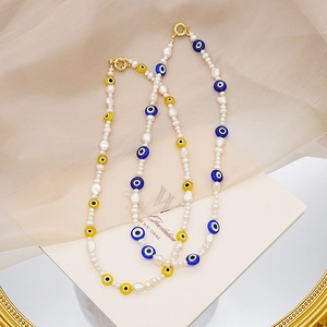 Detalle de collares de perlas barrocas con cuentas de ojo turco sobre bandeja dorada
