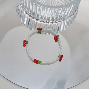 Détail du bracelet perlé cerise avec cristaux blancs et perles rouges sur une surface miroir