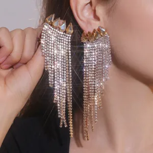 Close-up of long gold fringe earrings with amber teardrop stones and sparkling crystals