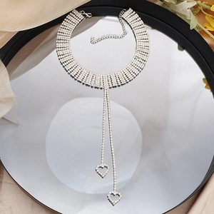 Detalle de gargantilla de pedrería plateada con borlas largas y dijes de corazón