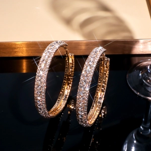 Overdreven gouden C-vormige oorringen met sprankelende strass-steentjes op zwarte basis
