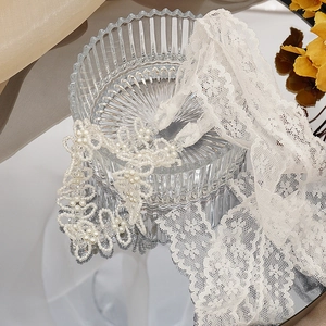 Dettaglio di fascia per capelli in pizzo bianco con perle e motivi floreali su seta