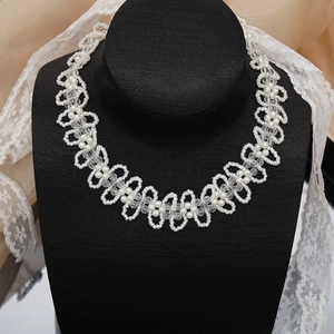 Dettaglio di collana in perle e cristalli intrecciata a mano su busto nero con pizzo