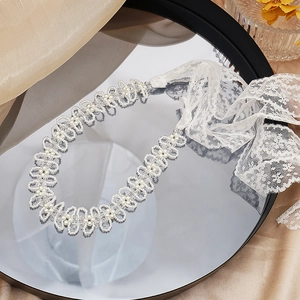 Dettaglio del girocollo in pizzo con perle e cristalli e nastro bianco regolabile
