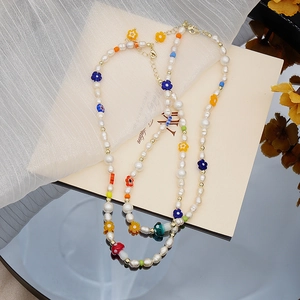 Détail d'un collier en perles d'eau douce avec fleurs en résine et perles dorées