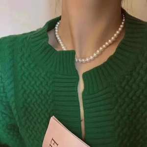 Close-up of white glass pearl necklace worn with a green knitted cardigan