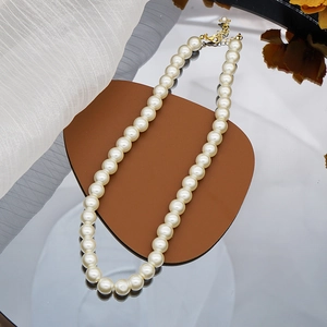 Detailed close-up of a white glass pearl necklace with a golden lobster clasp and chain