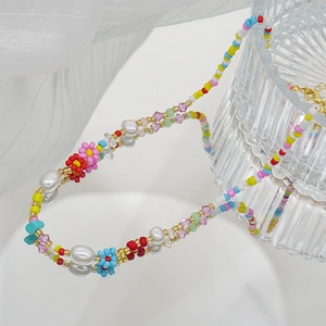 Détail d'un collier de perles colorées avec fleurs et cristaux sur tissu blanc élégant
