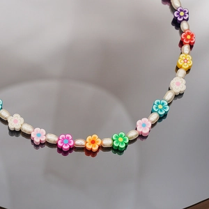 Gros plan de perles florales colorées et perles blanches sur un collier ras du cou