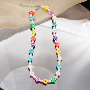 Détail de perles florales colorées et perles blanches sur un collier ras du cou perlé