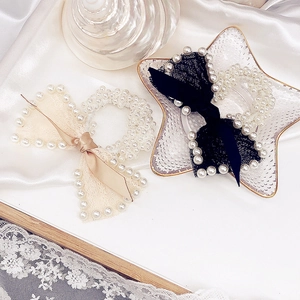 Detail of beige and black lace bow hair ties with faux pearl beads on silk background