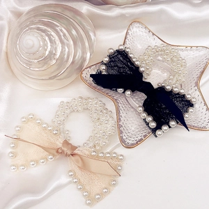 Close-up of pearl beaded hair ties with black lace and beige satin bows on silk