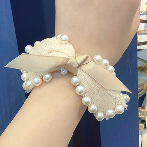 Detailed shot of a champagne satin bow hair tie with pearls worn on the wrist