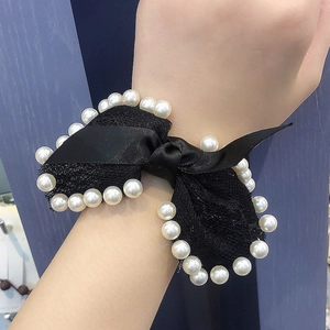 Detail of a black lace bow hair tie with white pearls worn on a wrist for styling