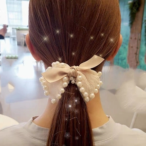 Detail of a creamy beige bow hair tie with lace edges and pearls worn on a ponytail
