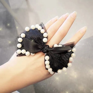 Detail of black lace bow hair tie featuring elegant pearls on a woman's hand