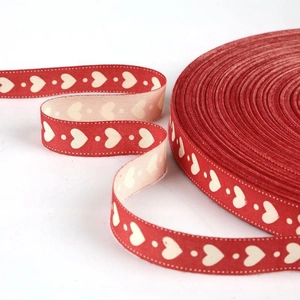 Detailed view of red cotton ribbon with white heart patterns and dotted decorative edges