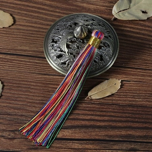 Dettaglio di una nappa di seta colorata con filo dorato su sfondo in legno scuro