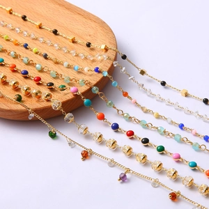 Detail of 18k gold plated chains with colorful beads and crystal charms on a wooden tray