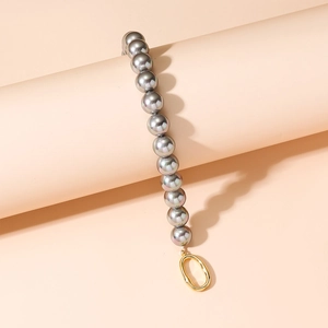 Bracelet de perles grises avec fermoir doré ovale sur un fond pêche chaud et minimaliste